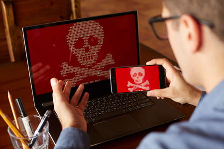 Man sits near laptop with phone blocked and encrypted by ransomware spyware asking for money. Laptop...