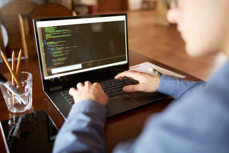 Back view over the shoulder shot of developer programmer with laptop. Program code and script data...