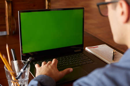 Back view of freelancer man in glasses working with laptop. Green screen. Caucasian businessman doing project on pc. Copyspace and product placement.の写真素材