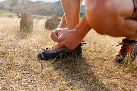 Close-up of unrecognizable man putting his orange climbing shoes on and binding shoelaces outdoors...
