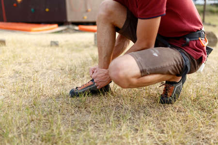 Close-up of unrecognizable man putting his orange climbing shoes on and binding shoelaces outdoors before rock climb training.の写真素材