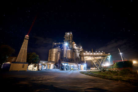 Grain terminal at seaport with starry sky on background. Cereals bulk transshipment from road transport to vessel at night. Loading grain crops on ship from elevators at the berth. Long exposure.の写真素材