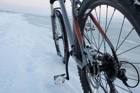 Mountain bike stay in snow near frozen sea or lake. Rear wheel shifter and disk breaks detail....