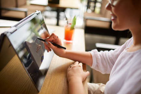 Businesswoman hand pointing with stylus on the chart over convertible laptop screen in tent mode. Woman using 2 in 1 notebook with touchscreen for work on business presentation. Isolated close view.の写真素材