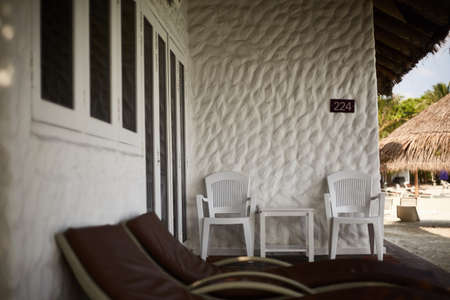 Two wooden lounge chairs and two arm chairs on the deck of garden bungalow in Maldives.