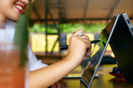 Isolated side view of freelancer woman hand pointing with stylus on convertible laptop screen in tent mode. Girl using 2 in 1 notebook with touchscreen for drawing and work on design project.の写真素材