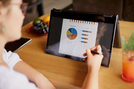 Businesswoman hand pointing with stylus on the chart over convertible laptop screen in tent mode. Woman using 2 in 1 notebook with touchscreen for work on business presentation. Isolated close view.の写真素材