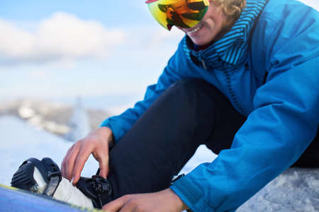 Snowboarder straps in his legs in snowboard boots in modern fast flow bindings with straps. Rider at ski resort prepares for freeride session and . Man wearing fashionable outfit. Feet close-up.の写真素材