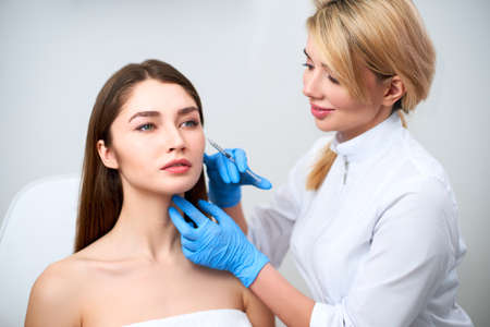 Beautician doctor with botulinum toxin syringe making injection to to remove crows feet. Cheek volume enhance mesotherapy. Anti-aging treatment and face lift in cosmetology clinic.の写真素材