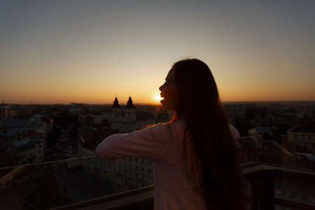Young beautiful woman admiring panoramic view of european street architecture high from the balcony....
