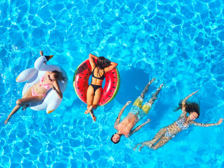 Aerial of friends having party in swimming pool with inflatable flamingo, swan, mattress. Happy young people relax at luxury resort on sunny day. View from above. Girls in bikini sunbathing in a sun.の写真素材