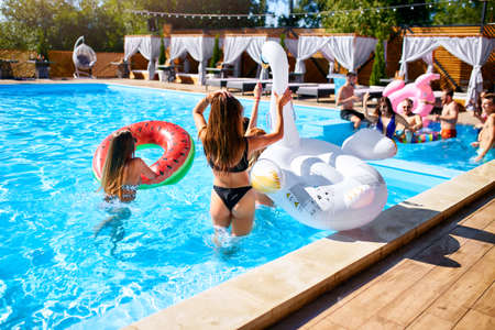 Hot pretty girls in bikini walking together with inflatable swan, swim ring into swimming pool....