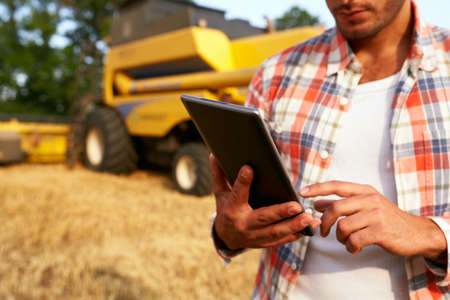 Precision farming. Farmer holding tablet for combine harvester guidance and control with modern automation system. Agronomist using online data management software generating yield maps at wheat fieldの写真素材
