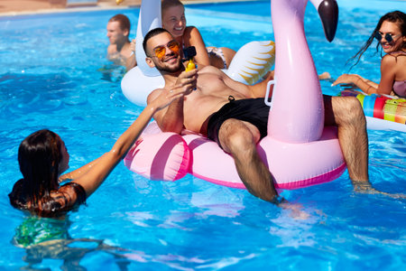 Travel blogger man taking selfie photo with action camera in a swimming pool. Lifestyle vlogger films vlog from luxury resort on sunny day. Fitted guy live streaming for social media likes.の写真素材