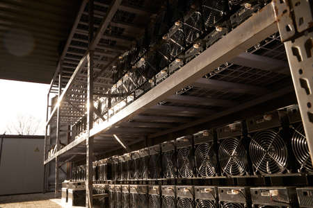 Bitcoin ASIC miners in warehouse. ASIC mining equipment on stand racks for mining cryptocurrency in steel container. Blockchain techology application specific integrated circuit units storage.の写真素材