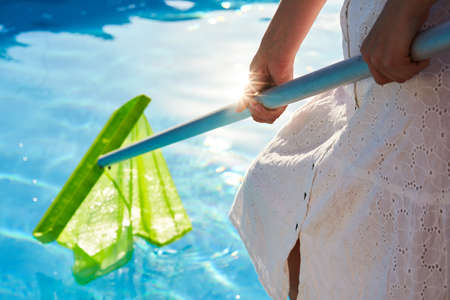 Woman with skimmer net equipment cleaning swimming pool from rubbish. girl removes garbage from the water with a sap. Swimming pool cleaning and maintenance service. Hotel cleaner.の写真素材