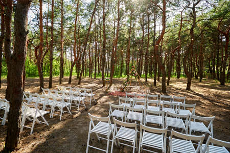 Beautiful bohemian tipi arch decoration on outdoor wedding ceremony venue in pine forest with cones. Chairs, floristic flower compositions of roses, carpet, string fairy lights. Summer rural wedding.の写真素材