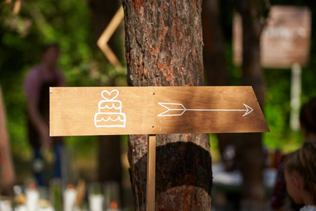 Decoratoration wooden wedding cake arrow sign in the pine forest. Cake banner on event venue in the woods outdoors.の写真素材