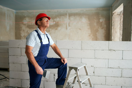 Professional construction worker in uniform standing with spatula on step ladder. Portrait of...