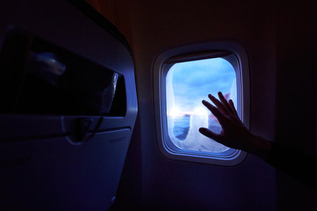 Female hand touches the warm sun rays from airplane window. Woman looking forward to travel on her vacation. Girl on a journey flight sitting in aircraft and enjoys sun flares.の写真素材