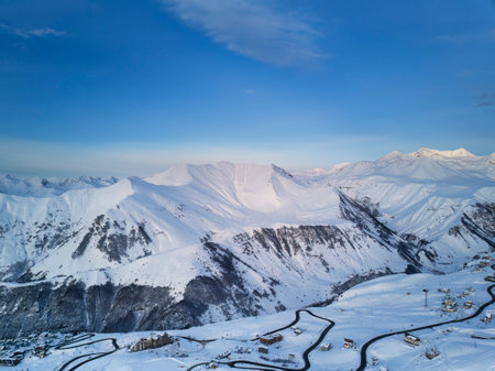 Wide aerial panorama of snowy mountain ridge at ski resort village on sunrise. Stunning mountains...