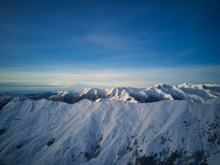 Wide aerial panorama of snowy mountain ridge at ski resort village on sunrise. Stunning mountains...