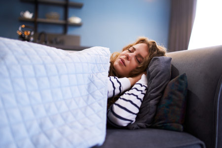 Girl sleeps on cozy sofa in living room at siesta time under a warm blanket. Sleeping woman taking...