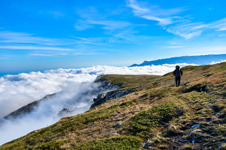 Silhouette of a man in the mountains. Successfully achieving goals. Male hiker on mountain peak with green grass looking at beautiful mountain valley at sunset against clear blue sky..の写真素材