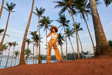 Young african female model posing in colorful clothes at tropical location at sunrise. Black woman against exotic scenery at dawn. Multiracial dark-skinned model poses in front of palm trees at sunsetの写真素材