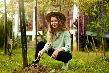 Young happy farmer woman in straw hat sitting in garden taking care of her plants and harvest. Young...