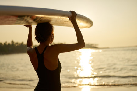 African american woman standing with surfboard on her head on ocean beach. Black female surfer...