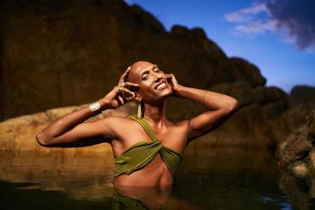 Happy trans sexual fashion model shows golden jewelry chest deep inside natural pool surrouded by...