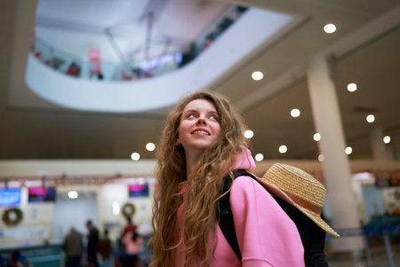 Smiling tourist with backpack gazes upward in bustling airport decorated for festive season, ready to embark on a winter vacation.の写真素材