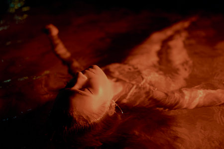 Woman reclines gracefully in water at night, her form bathed in dim, warm light, creating a tranquil, serene scene. The photo of femininity, allure, natural element beauty, sense of creative art.の写真素材