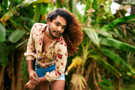 Confident gay man with curly hair in tropical setting poses with style, ethnic LGBTQ individual in...
