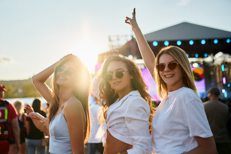 Friends enjoy sunset at beach music fest. Girls dance, laugh in summer vibe. Group celebrates at...