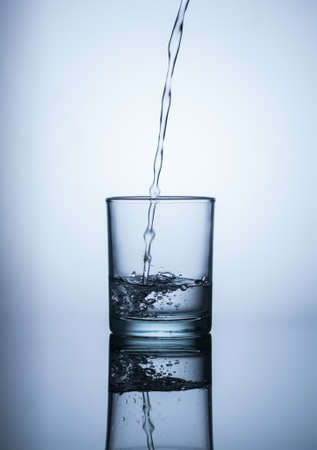 Water flows into the glass and makes bubbles on blue backgroundの写真素材