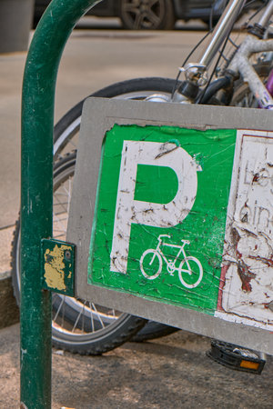 Detailed close-up of an old green bicycle parking sign with peeling paint, white âPâ and bike silhouette, showing part of a parked bicycle and green metal stand in the background.の写真素材