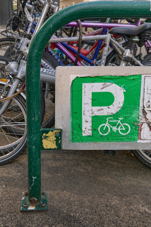 Wide-angle view of a worn green bicycle parking sign mounted on metal stand, showing numerous bicycles tightly parked in the background on a city street.の写真素材