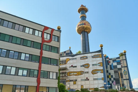 Close-up of Vienna's Spittelau waste-to-energy plant designed by Hundertwasser. Bright facade with many windows, golden dome chimney and blue summer sky.の写真素材