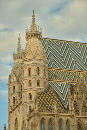 View of St. Stephen's Cathedral in Vienna featuring its colorful mosaic roof and front spires against a partly cloudy sky, highlighting Gothic architecture.の写真素材