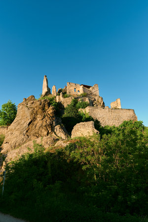 Scenic view of a hill with ancient castle ruins and stone walls overgrown with greenery under a clear blue sky in Wachau Valley, Austria on a sunny day.の写真素材