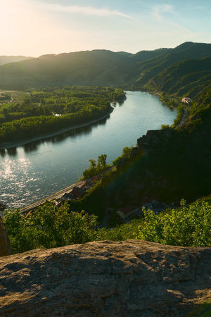 Vertical aerial view of sun-drenched hills and Danube River in Wachau Valley, Austria. Scenic landscape with forested slopes and bright golden sunlight on a clear summer day.の写真素材