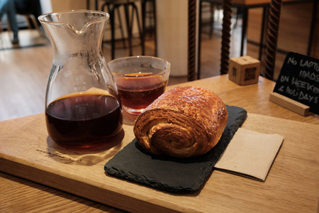 Chocolate swirl pastry placed on stone stand, with glass carafe and small cup of filtered coffee on...