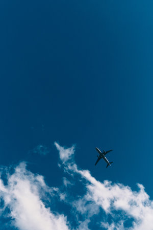 View from the ground of a large airplane flying low across a bright blue sky with white clouds....