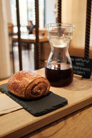 Fresh pastry on black stone stand with glass coffee carafe on wooden tray, on wooden table with...