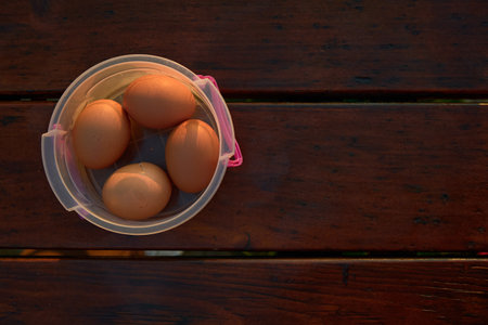 Simple boiled eggs placed in a small plastic container on a rustic outdoor table. Natural light...