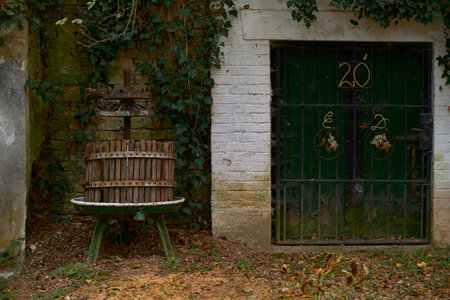 Historic wine press stands near green door with wrought iron grapevine design and number 20....