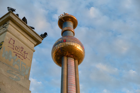 Horizontal shot of Vienna's Spittelau plant showing part of the sculptural bridge-like structure, pigeons, and graffiti, with the tower and golden dome visible in the background.の写真素材