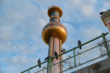 Horizontal shot of pigeons perched on a railing with Vienna's Spittelau copper dome in the background. Blue sky and soft light highlight the architecture and urban wildlife.の写真素材